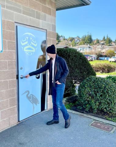 A man in a black beanie opening a door with a heron and First Nations art design.