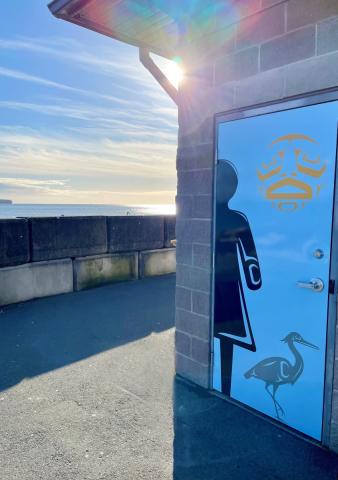 Sunlight reflecting off the ocean next to a building with a door decorated with First Nations art.