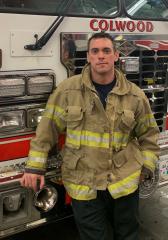 Firefighter in uniform standing in front of a Colwood fire truck.