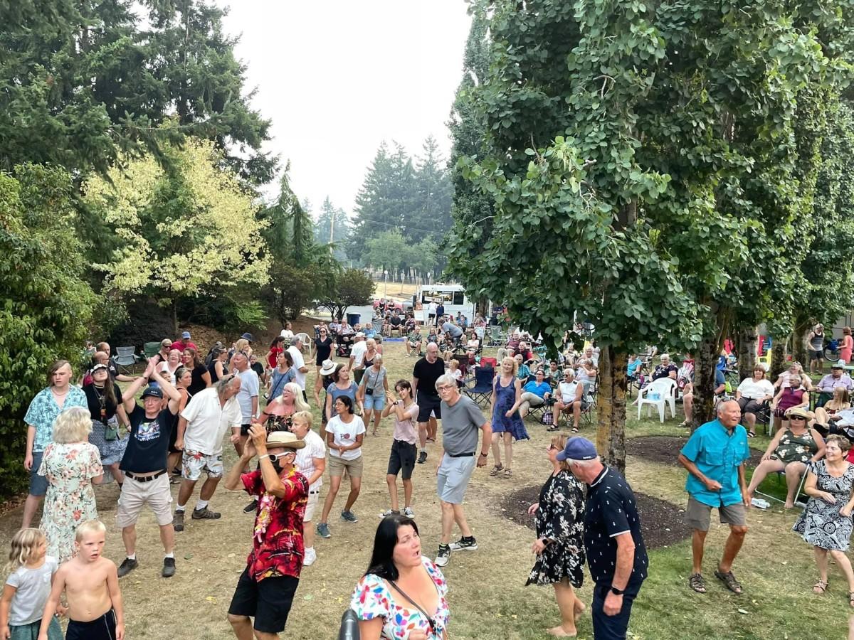 A large crowd of people enjoying an outdoor event with music and dancing in a wooded area.