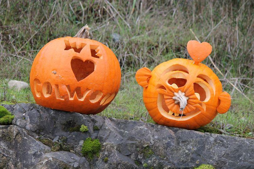 Two carved pumpkins on a rock, one with 'We ♥ Colwood' and the other with a smiling face and a heart-shaped nose.