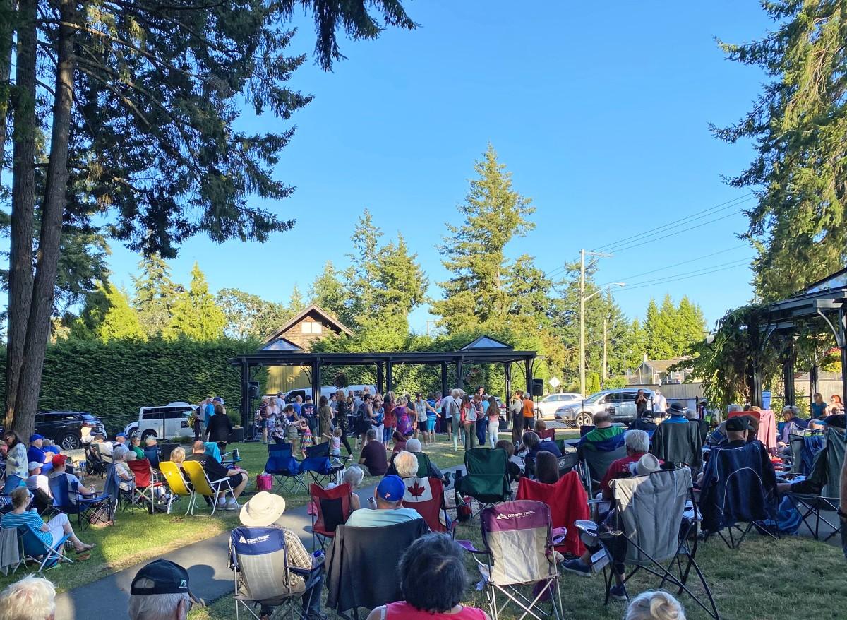 Outdoor event with a large crowd seated in chairs, enjoying a performance or gathering on a sunny day.