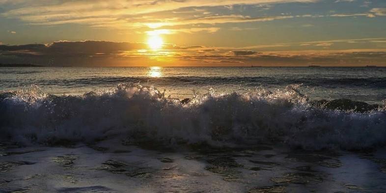 Ocean waves crashing under a sunset sky, creating a dramatic scene with the sun low on the horizon.