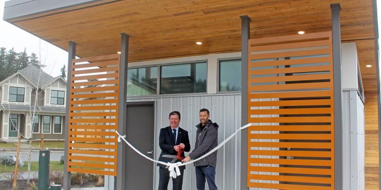 Two men cutting a ribbon at the opening of a modern building with wooden slats and metal siding.