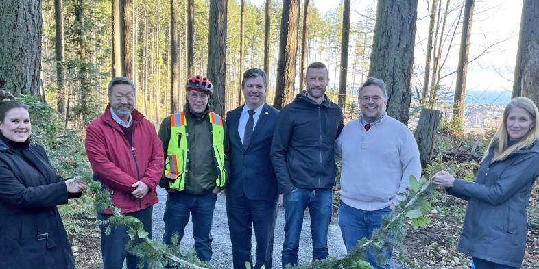 Group of people, including local officials, standing in a forested area for a ribbon-cutting ceremony.