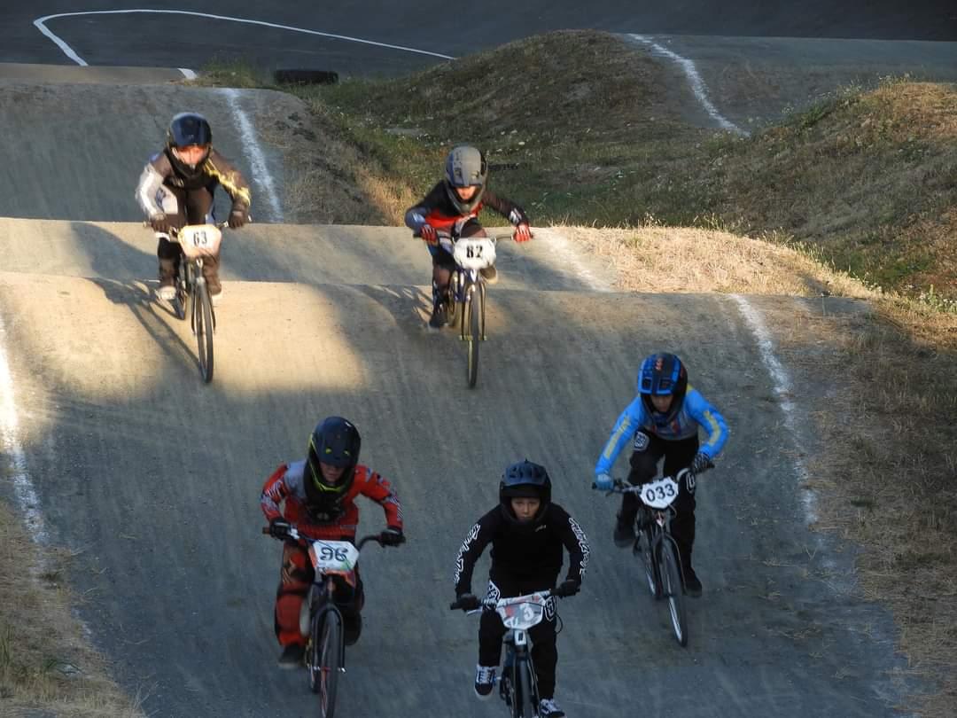 Five young BMX riders in racing gear competing on a dirt track with an incline.