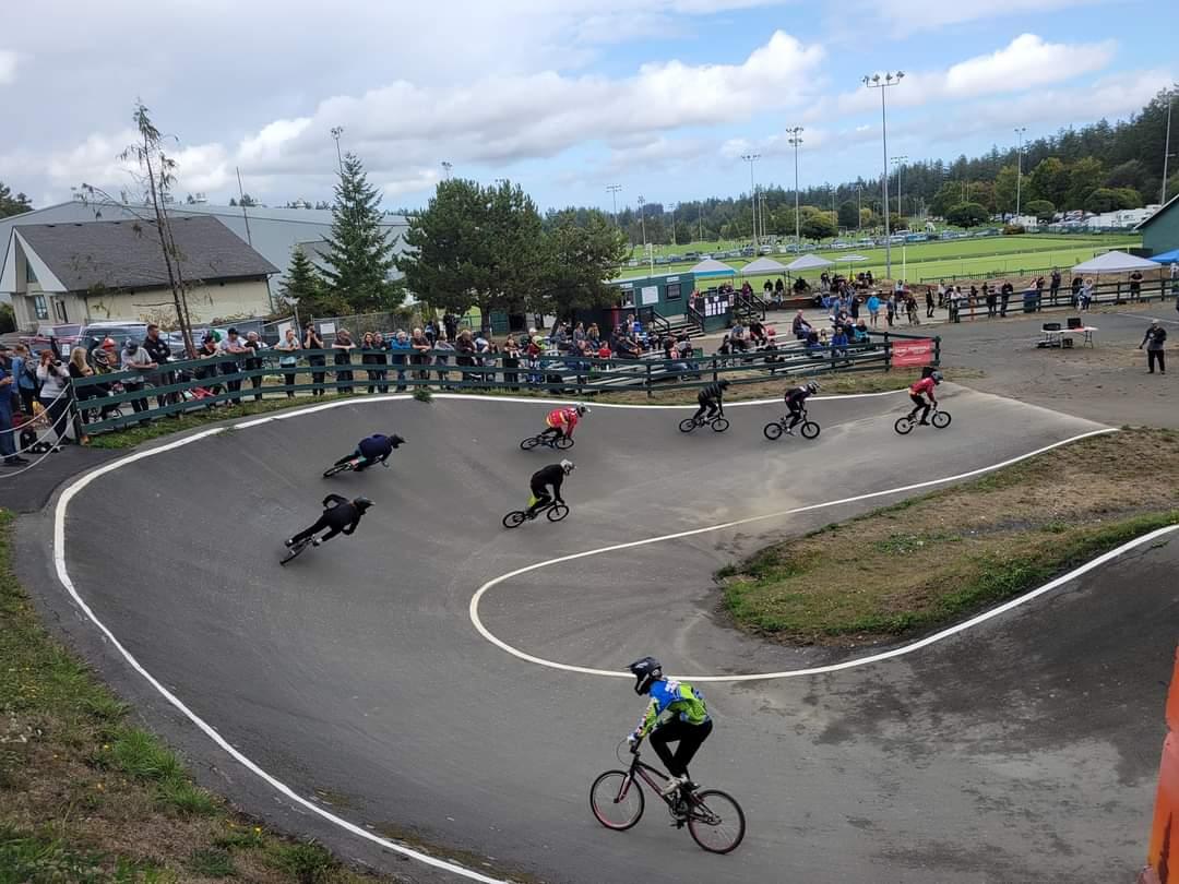 BMX riders racing on a curved track with spectators watching from the sidelines.