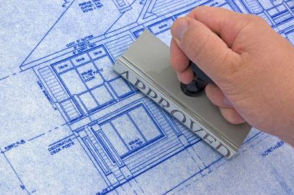 Close-up of a hand stamping a large "APPROVED" mark on a blueprint of a house.