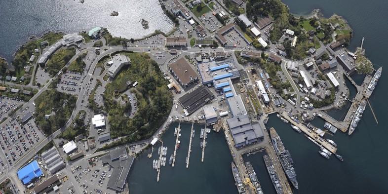 Aerial view of a coastal town with docks, boats, buildings, and parking areas near the water.