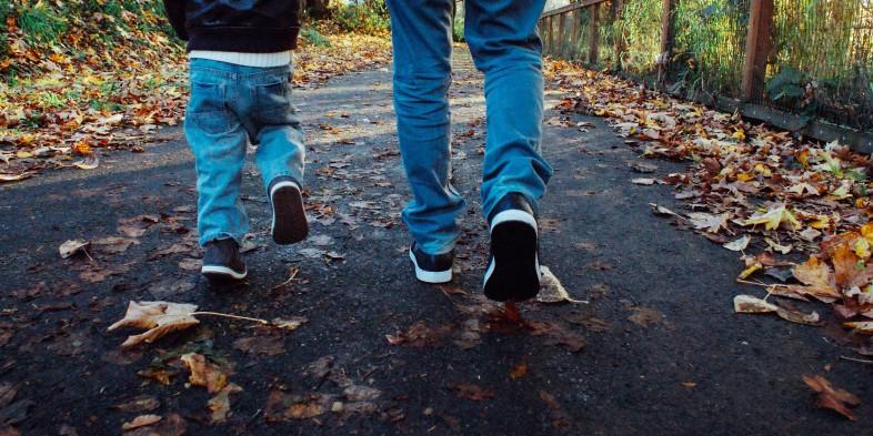 A child and an adult walking on a leaf-covered path.