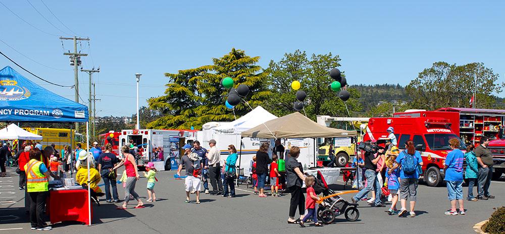 Community event with various emergency service booths and vehicles, attended by families and children.