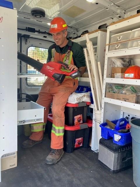 Utility worker in orange overalls and a hard hat organizing tools inside a work van.