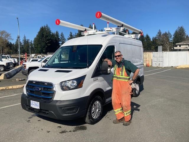 Utility worker in orange overalls posing next to a Colwood Zero Emission Fleet Vehicle.