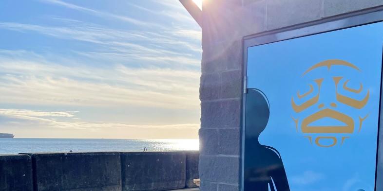 Sunlight reflecting off the ocean next to a building with a door decorated with First Nations art.