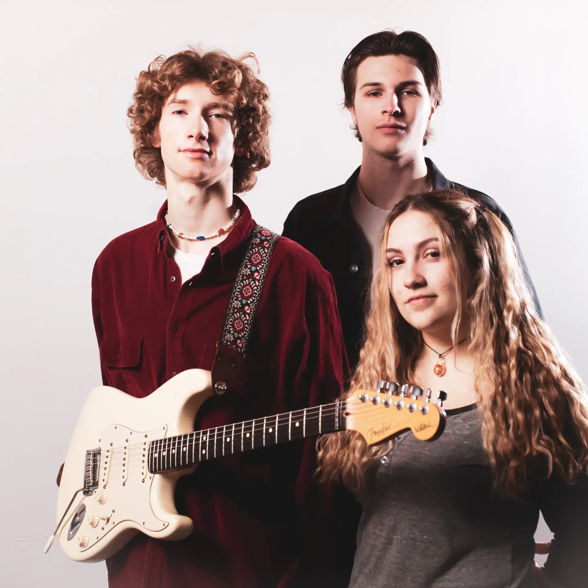 Three young musicians posing together, with one holding an electric guitar.