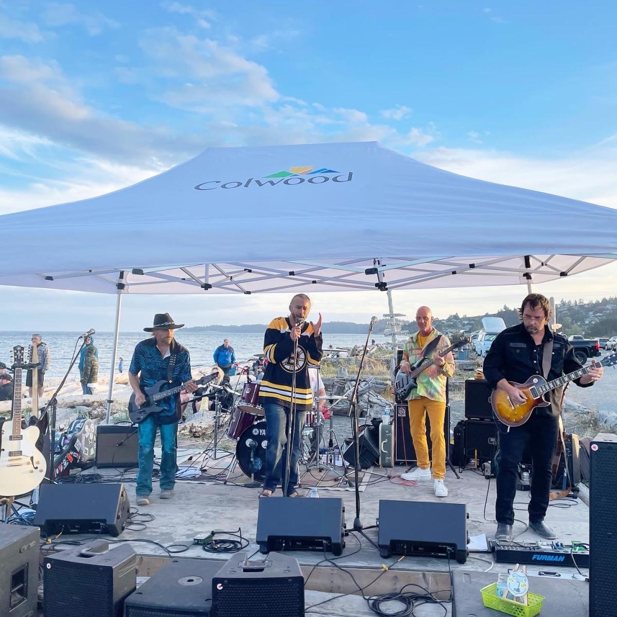 A band performing under a Colwood-branded tent on a beach with the ocean in the background.