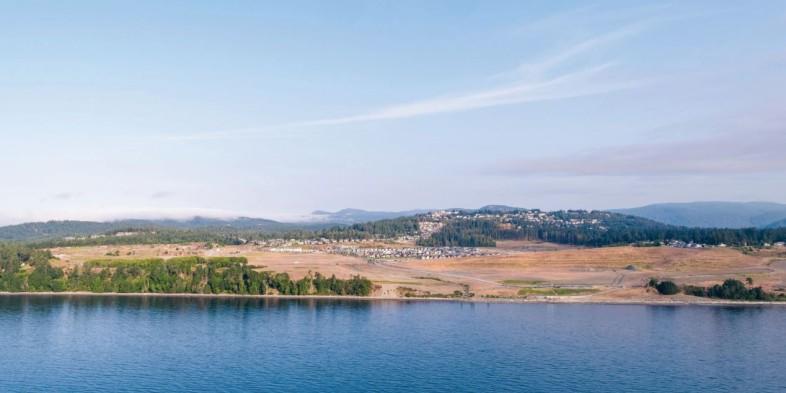 Panoramic view of a waterfront community with houses and green spaces in the background.