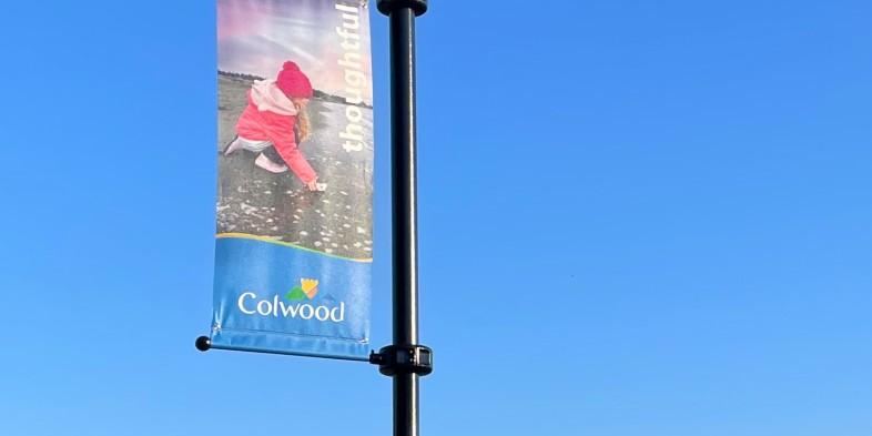 A street banner with a child playing on the beach, and the text "thoughtful" and "Colwood" against a clear blue sky.